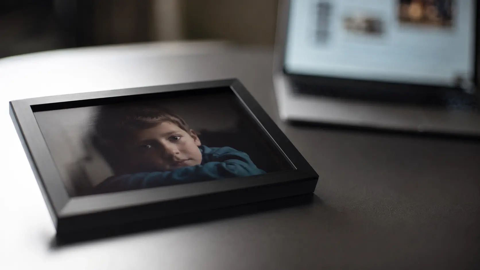 Ausgedrucktes Kinderfoto auf einem Tisch, im Hintergrund ein leuchtender Laptop-Bildschirm